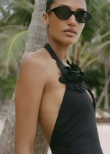 Traje de baño enterizo negro con escote halter y detalle de flor aplicada en el frente. Presenta espalda descubierta y cierre de lazo en el cuello.