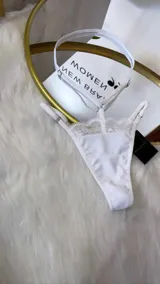 Tanga de lycra blanca con detalles de encaje en la parte superior y tiras laterales regulables.