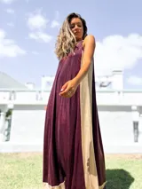 Vestido largo de fiesta con diseño bicolor, presentando un panel frontal en color bordó y paneles laterales en color dorado. Confeccionado en tela brillante con caída fluida, presenta escote halter y corte holgado.