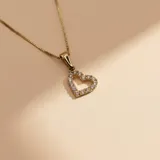 Conjunto de cadena fina y dije en forma de corazón calado, engastado con pequeñas circonias brillantes. Fabricado en oro 10k.