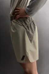 Pantalón corto de trail running color beige, confeccionado en tejidos técnicos ligeros y elásticos. Cuenta con forro interior, cintura elástica ajustable con cordón, bolsillos traseros laterales multifunción, bolsillo trasero central con cremallera, bajo con costura termofijada y aberturas laterales. Incluye logo estampado en la pernera.