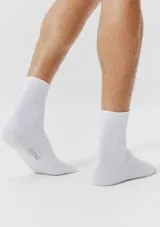 Kit de tres pares de medias unisex de caño medio, confeccionadas en tejido suave y elástico de color blanco, con el logo de la marca estampado en la planta del pie.