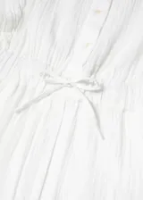 Mono largo de tejido de bambula con textura, color blanco. Presenta cuello de tira, cierre frontal con botones, mangas cortas con hombreras sutiles y cintura elástica con lazo ajustable.