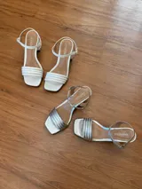 Sandalias de tacón cuadrado medio, con diseño de tiras finas y cierre de pulsera ajustable al tobillo. Confeccionadas en cuero sintético, presentan una punta cuadrada y un estilo minimalista y versátil.