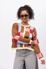 Saco tipo cardigan de tejido de punto con diseño geométrico de cuadros en tonos marrón, celeste, rosa y rojo. Presenta cuello redondo, cierre frontal con botones y terminaciones en color crema.