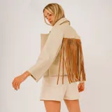 Campera de cuero beige con solapas amplias y flecos largos de cuero marrón en la espalda.