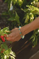 Pulsera elástica combinada con cuentas metálicas doradas en forma de barril y cristales facetados de color turquesa.