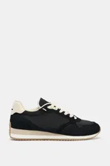 Zapatilla deportiva tipo running con diseño de paneles en contraste. Presenta cuerpo en color negro con refuerzos de gamuza sintética, detalle de pespuntes, talón en color crema y suela dentada bicolor.