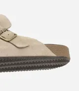 Ojota mule color beige confeccionada en cuero, con tira ancha y hebilla metálica.