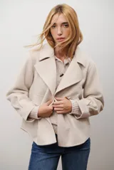 Chaqueta corta de paño color beige, con cuello solapa, cierre frontal mediante alamar y bolsillos delanteros. Presenta un corte estructurado y mangas largas.