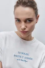 Remera blanca de silueta amplia y calce relajado, confeccionada en tela suave y liviana, con cuello redondo, mangas cortas con vuelta y hombros caídos. Cuenta con un delicado bordado frontal en color azul con la inscripción "LE SOLEIL TOUTE L'ANNÉE sur la Côte d'Azur".