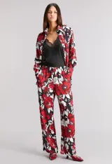 Pantalón pijamero de satén calado estampado con flores rojas y blancas sobre fondo negro, de calce relajado, cintura elastizada y bolsillos ocultos.