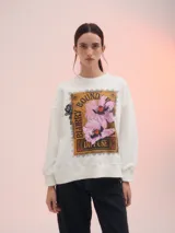 Buzo blanco de corte clásico con estampa rectangular centrada en el frente con flores rosadas y texto en color ocre.