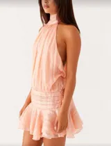 Vestido corto color naranja, con cuello halter, espalda descubierta y falda con volados. Presenta pliegues en la cintura.