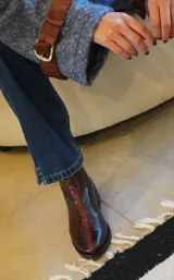 Botín negro de cuero liso, con puntera fina y taco bajo. Presenta costuras decorativas en hilo color crudo y cierre lateral con tirador.