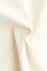 Top de manga larga color crema, confeccionado en punto suave de algodón, con escote bote y hombros caídos. Presenta un calce entallado en la cintura y mangas largas amplias.