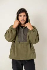 Canguro con capucha de estilo urbano en color verde oliva, confeccionado en tejido suave. Presenta un panel frontal en contraste de color gris oscuro con cierre de cremallera parcial, mangas largas con puños elásticos y bolsillos laterales integrados.