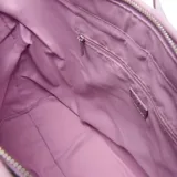 Cartera tipo tote de diseño estructurado, confeccionada con tejido efecto rafia en color beige y detalles de cuero sintético en tono lila. Cuenta con asas largas de hombro ajustables con hebillas y una pequeña placa metálica con el logo de la marca en el frente.