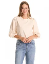 Blusa color beige con bordado floral al tono en el pecho y la espalda. Presenta mangas largas abullonadas con frunces en los hombros y puños festoneados. El ruedo cuenta con un acabado festoneado en ondas y la espalda incluye una abertura tipo gota con cierre de botón.