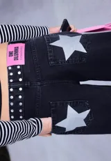 Jean de corte recto y tiro bajo, color negro, con detalle de tachas metálicas en la cintura y una banda lateral de brillos a lo largo de la pierna.