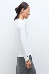 Remera de manga larga color blanco, con cuello redondo y detalle de botones en los puños.
