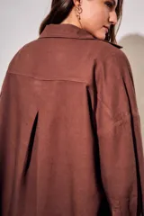 Camisa oversize color marrón, confeccionada en mezcla de viscosa y lino, con cuello clásico, cierre frontal con botones y un bolsillo aplicado en el pecho.