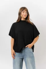 Sweater de tejido de punto color negro, con cuello semi alto y mangas cortas amplias. Presenta una silueta relajada y caída fluida.