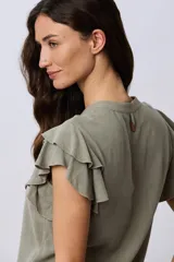 Camisa de lino y viscosa color beige, con cuello mao, escote en V y botones frontales de madera. Presenta mangas cortas con volados delicados.