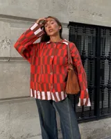 Saco tejido de punto con diseño de cuadros en tonos rojo, marrón y rosa claro. Presenta corte recto oversize, cierre frontal con botones en forma de corazón y dos bolsillos delanteros.