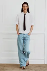 Camisa de algodón de corte recto con cuello solapa, manga corta y cierre frontal con botones ocultos. Presenta un diseño con pechera y una corbata negra extraíble a contraste.