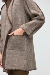 Tapado liviano de corte relajado, confeccionado en lana fina sin teñir. Presenta un diseño abierto con terminaciones artesanales en crochet a lo largo de los bordes y bolsillos frontales aplicados.
