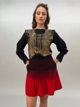 Remera negra de algodón con estampado dorado que simula un tejido o collar sobrepuesto. Presenta una moldería que realza los hombros y se entalla levemente hacia la cintura.