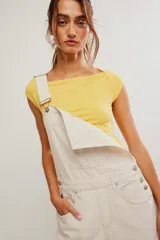 Jardinero de denim color blanco crudo, con peto, tiras ajustables y botones metálicos. Presenta diseño de pierna amplia tipo barrel, bolsillos frontales y traseros, con costuras pespuntadas visibles.
