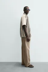 Camisa de manga corta con calce relaxed fit, confeccionada en tejido estructurado con algodón. Presenta un diseño de rayas verticales en tonos beige, negro y blanco, cuello solapa, cierre frontal con botones y aberturas laterales en el bajo.