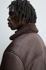 Cazadora oversize de efecto piel color negro, con interior y cuello solapa de pelo sintético gris a contraste. Cuenta con bolsillos de vivo en la cadera, acabados en rib elástico y cierre frontal con cremallera.