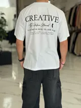 Remera oversize color beige, con diseño estampado en la espalda que incluye tipografía grande y texto descriptivo en negro.