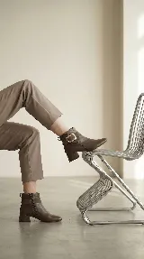 Bota corta de cuero con taco cuadrado bajo y punta redondeada. Presenta una tira decorativa en el tobillo con una hebilla metálica rectangular. Cuenta con cierre lateral interno para facilitar el calce.