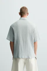 Camisa de manga corta con cuello solapa, confeccionada en tejido de mezcla de lyocell con textura de efecto arrugado y cierre frontal de botones.
