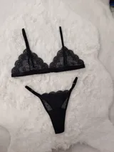 Conjunto de lencería de encaje negro, compuesto por un soutiene triangular de tirantes finos y una bombacha colaless ajustable con tiras laterales.