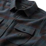 Camisa de manga larga con diseño a cuadros en tonos azul y negro, confeccionada en una mezcla de algodón y poliéster. Presenta cuello clásico, cierre frontal con botones y dos bolsillos en el pecho con solapa.