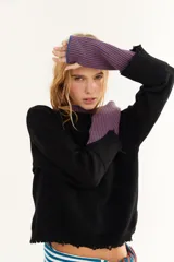 Sweater de punto color marrón con detalles en rojo en el cuello y los puños. Presenta un diseño de doble capa en el cuello y mangas largas con orificios para los pulgares, además de un pequeño bordado en el pecho y un acabado desflecado en el ruedo.