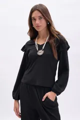 Blusa negra de manga larga con textura, cuello en V y detalle de volados en los hombros. Presenta mangas con puños elásticos y un corte recto.