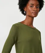 Suéter de punto color rosado, con cuello barco, mangas largas y puños con botones decorativos. El dobladillo también es acanalado.