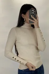 Polera de hilo blanca de cuello alto y manga larga, con detalle de botones dorados en los puños. Tejido de punto acanalado ajustado al cuerpo.