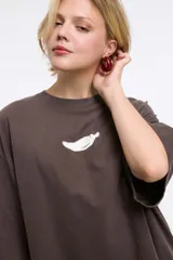 Remera de corte boxy color gris oscuro, con cuello redondo y mangas cortas. Presenta un diseño estampado localizado en la parte superior del pecho.