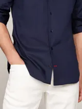 Camisa de manga larga para hombre, color azul marino, de corte slim fit, confeccionada en popelina con tecnología flex que incluye algodón orgánico. Presenta cuello con botones y el logo de Tommy Hilfiger bordado en el pecho.