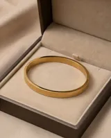 Pulsera tipo esclava rígida de acero con baño de oro, con diseño grabado de guarda griega en toda su superficie.