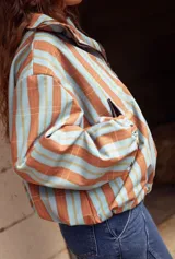 Campera impermeable con cierre frontal, diseño de rayas verticales en tonos celestes y marrones, cuello alto y puños elásticos.