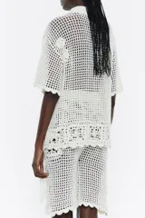 Camisa de crochet color blanco, con cuello camisero, manga corta y cierre frontal con botones.