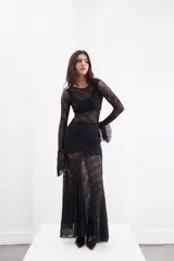 Vestido largo de encaje negro con transparencias, corte ajustado al cuerpo, mangas largas con terminación acampanada y falda con caída fluida.